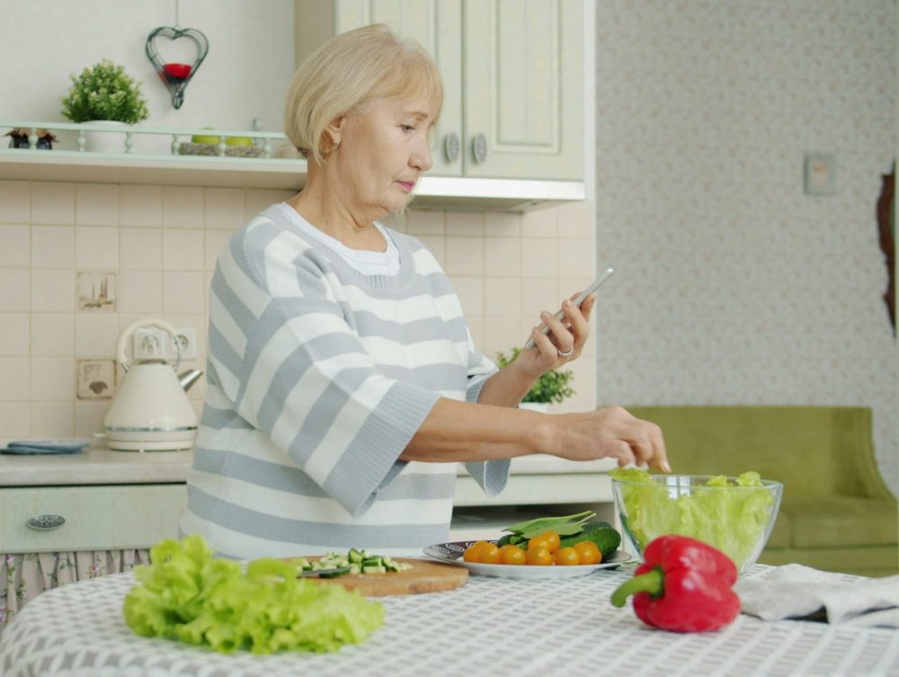 Vrouw die bezorgd naar haar telefoon kijkt terwijl ze kookt.